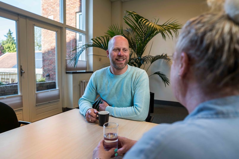 Twee ENRA medewerkers ingesprek aan een tafel op kantoor.