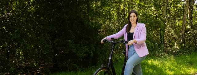 Dame op een elektrische fiets op een bospaadje, staat stil naast de fiets.