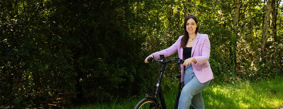 Dame op een elektrische fiets op een bospaadje, staat stil naast de fiets.