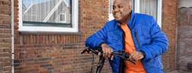 Man voor een pand leunt op het stuur van zijn e-bike en lacht.