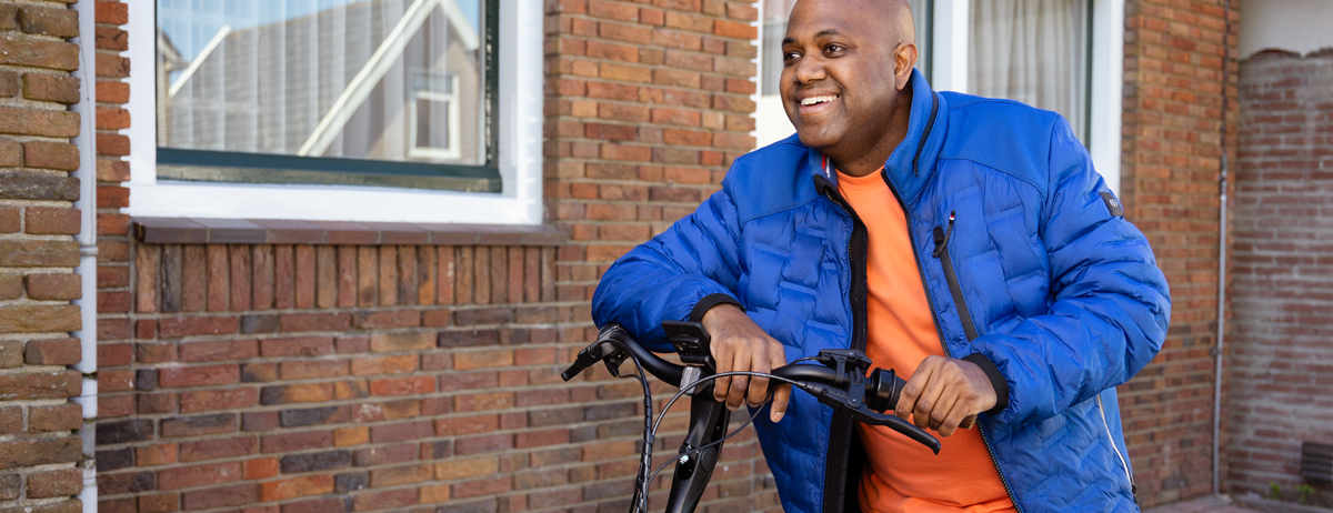 Man voor een pand leunt op het stuur van zijn e-bike en lacht.