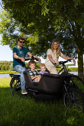 Man en vrouw op bakfiets en normale fiets met 2 kinderen in de bakfiets onder een boom