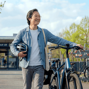 Man met zijn helm onder zijn ene arm en fiets in zijn andere hand loopt weg bij het station.