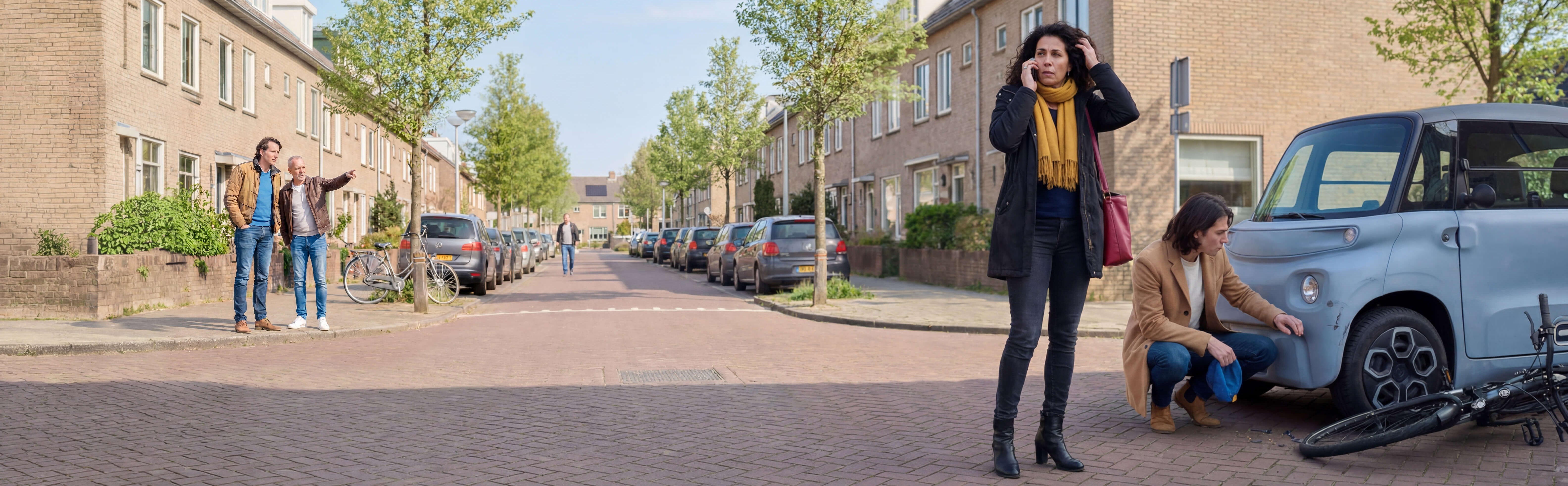 Een mevrouw belt de hulpdienst na een aanrijding tussen een fiets een brommobiel, de bestuurder van de brommobiel bekijkt de schade.