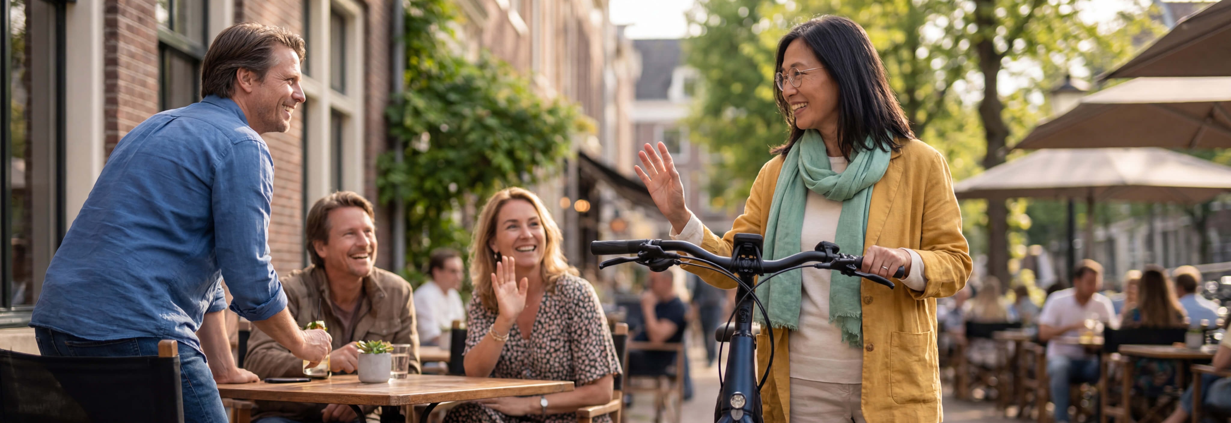 Een vrouw met een fiets loopt langs bekenden op een terras.