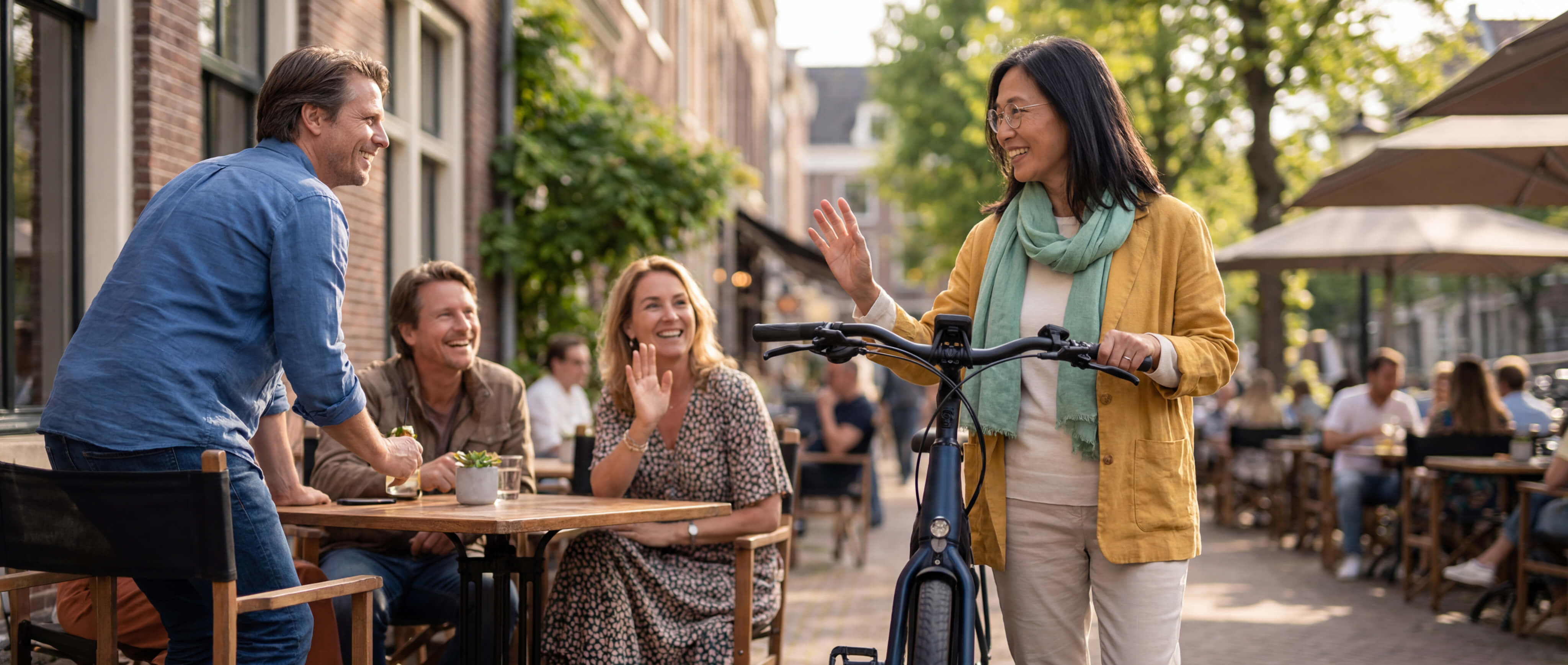 Een vrouw met een fiets loopt langs bekenden op een terras.
