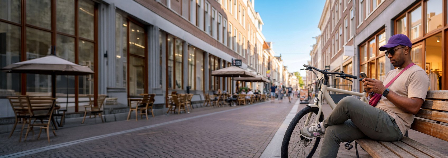Een man op een bankje met een telefoon in zijn handen en zijn fiets naast het bankje.