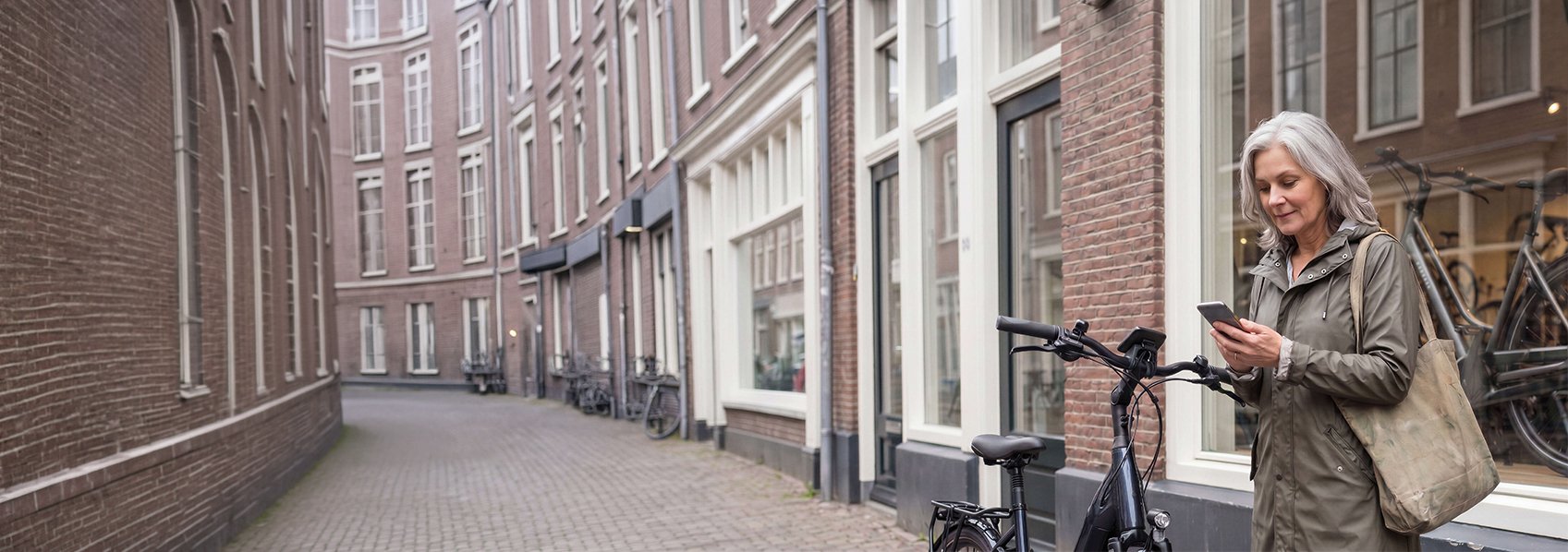 Een mevrouw staat met haar fiets voor de fietsenwinkel en geeft iets door via haar mobiele telefoon.